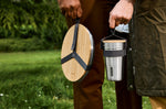 A close up of an adult holding the Black + Blum stainless steel plate and cup set by the handy black strap handle