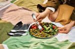A close up of an adult holding a spork and eating off the Black + Blum stainless steel plate