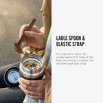 An image along side text. A close up of an open Black + Blum insulated stainless steel food flask with food inside. The text reads, ladle spoon and elastic strap. The ergonomic spoon fits snugly against the body of the flask, secured by an elastic and machine-washable strap. 