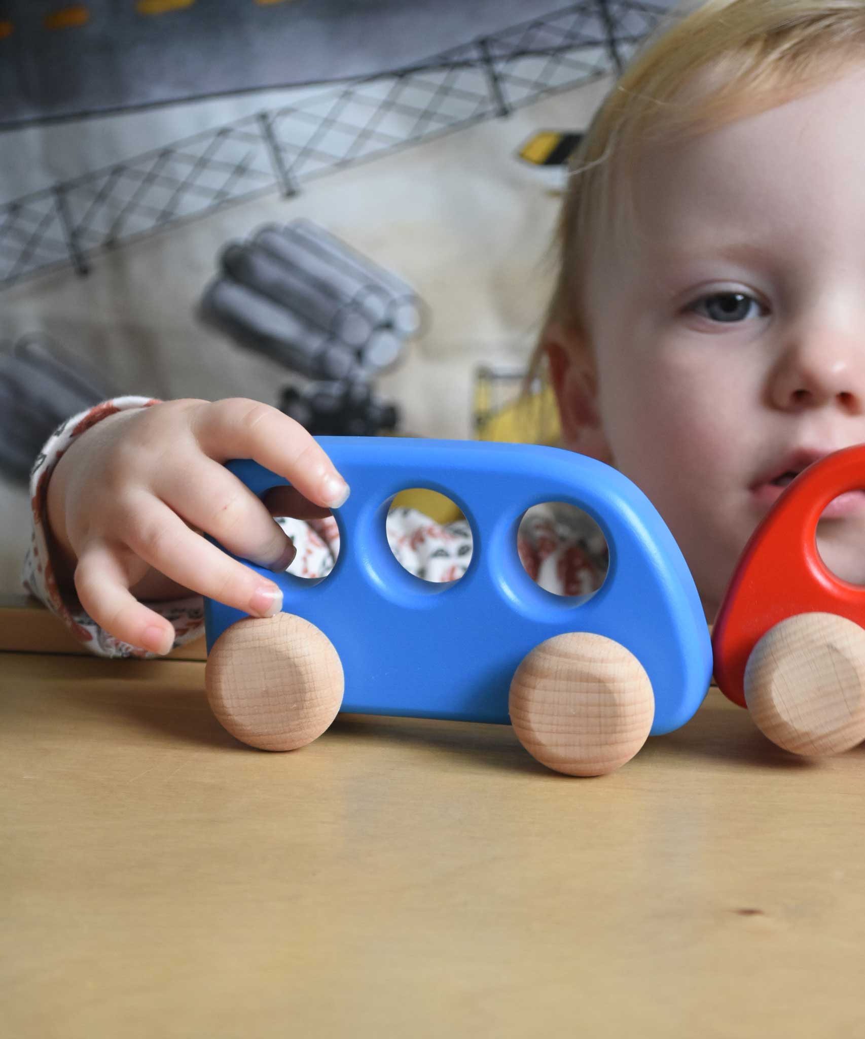 A child's hand pushing a blue coloured Bajo bus on a Triclimb Miri board. These heirloom quality toys by Bajo are part of a wide range of wooden toys available here at Babipur. 