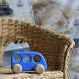 A blue coloured Bajo bus push along toy  placed on a child's wicker chair. These heirloom quality toys by Bajo are part of a wide range of wooden toys available here at Babipur. 