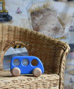 A blue coloured Bajo bus push along toy  placed on a child's wicker chair. These heirloom quality toys by Bajo are part of a wide range of wooden toys available here at Babipur. 