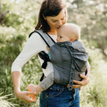 A parent outside in front of trees, carrying their child in the Boba Air Baby Carrier Ultra Lightweight - Grey