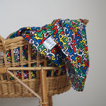 A baby graping and looking at the Etta Loves X Keith Haring Extra Large Organic Cotton Baby Muslin Square - Brazil