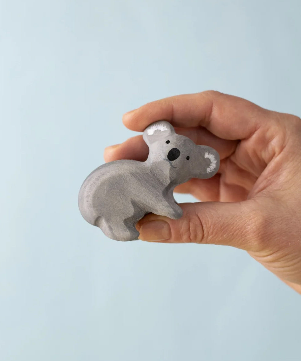 A Handmade Bumbu Toys Koala wooden figure in an adult's hand. 