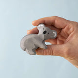 A Handmade Bumbu Toys Koala wooden figure in an adult's hand. 