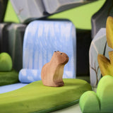 Bumbu Toys Wooden Sitting Baby Capybara in a scene with Bumbu rocks and grass.
