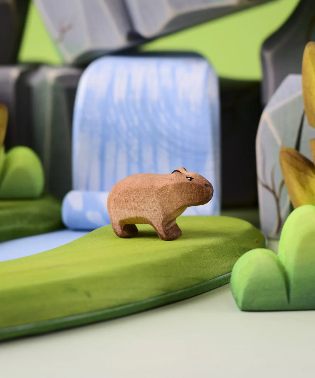 Bumbu Toys Wooden Baby Capybara in a scene with Bumbu rocks and grass.