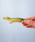 Bumbu Roys' Wooden Baby Crocodile, being held in an adult's hand.