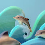 A Bumbu baby wooden dolphin perched on a wooden wave.