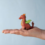 A Bumbu Toys Baby Dragon wooden figure placed in an adult's palm to show scale. 