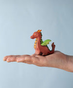 A Bumbu Toys Baby Dragon wooden figure placed in an adult's palm to show scale. 