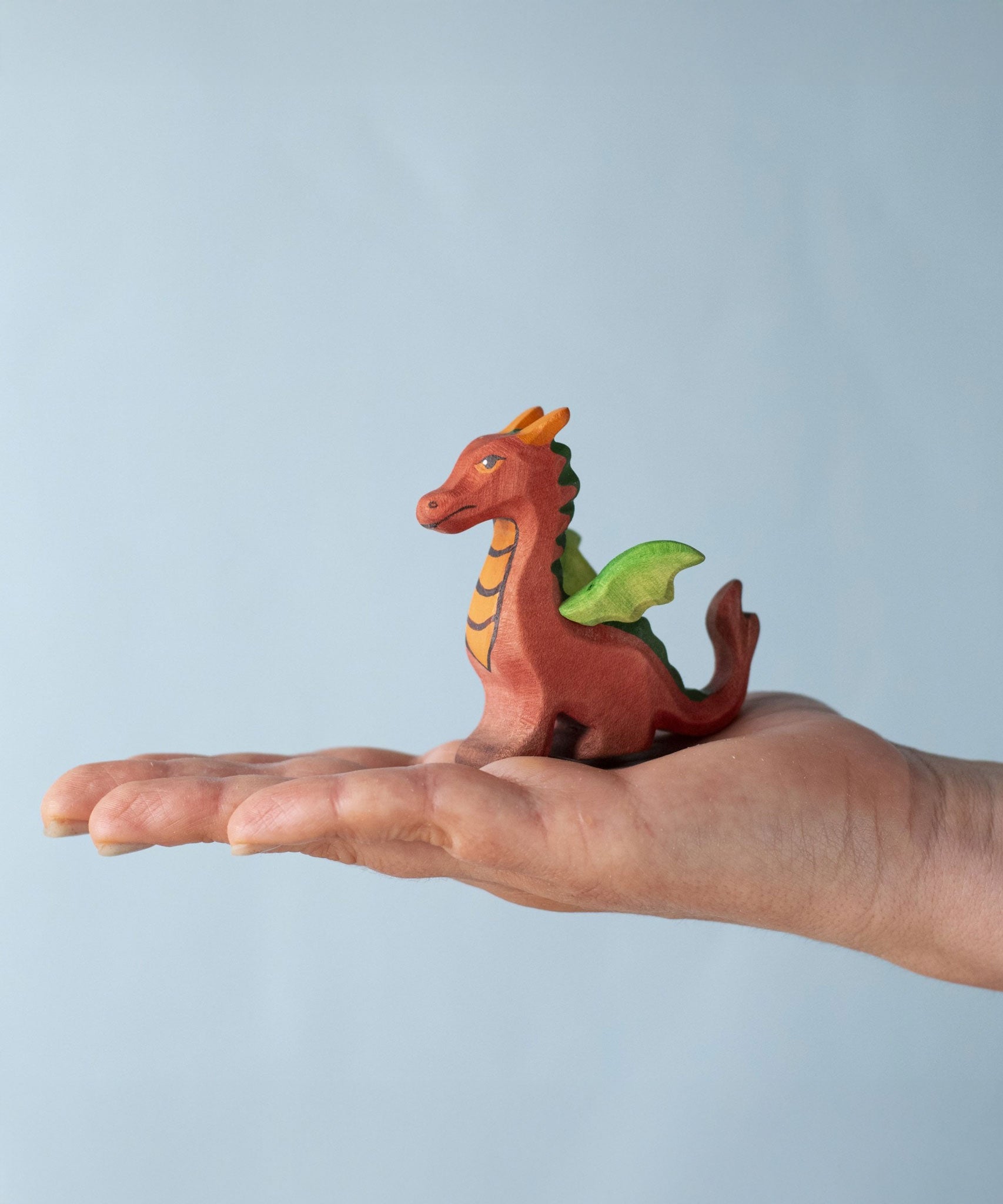A Bumbu Toys Baby Dragon wooden figure placed in an adult's palm to show scale. 