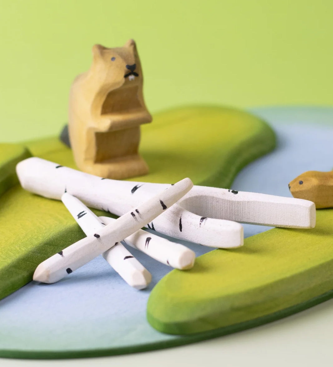 A play scene featuring Bumbu beaver figures standing next to a stack of birch branches on top of a river base.