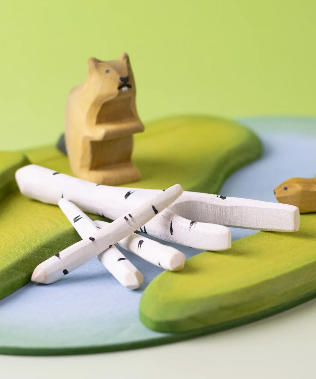 A play scene featuring Bumbu beaver figures standing next to a stack of birch branches on top of a river base.