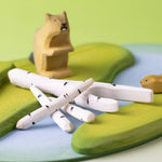 A play scene featuring Bumbu beaver figures standing next to a stack of birch branches on top of a river base.