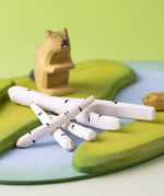 A play scene featuring Bumbu beaver figures standing next to a stack of birch branches on top of a river base.