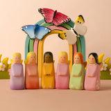 A playscene showing all Bumbu wooden fairy figures in front of a rainbow with butterflies and blossom bushes.