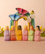 A playscene showing all Bumbu wooden fairy figures in front of a rainbow with butterflies and blossom bushes.
