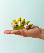 Adult hand holding a Bumbu wooden blossom bush figure showing scale