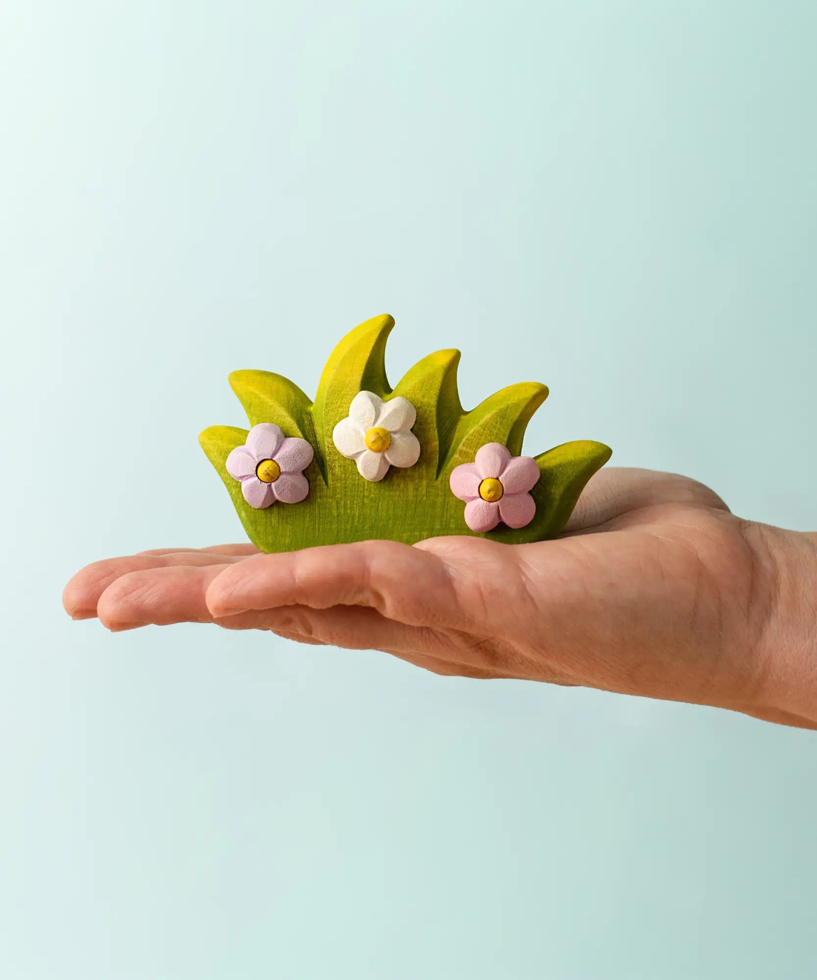 Adult hand holding a Bumbu wooden blossom bush figure showing scale