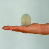 Adult hand holding the Bumbu handcrafted festive blue egg decorative figure showing size