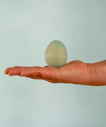 Adult hand holding the Bumbu handcrafted festive blue egg decorative figure showing size