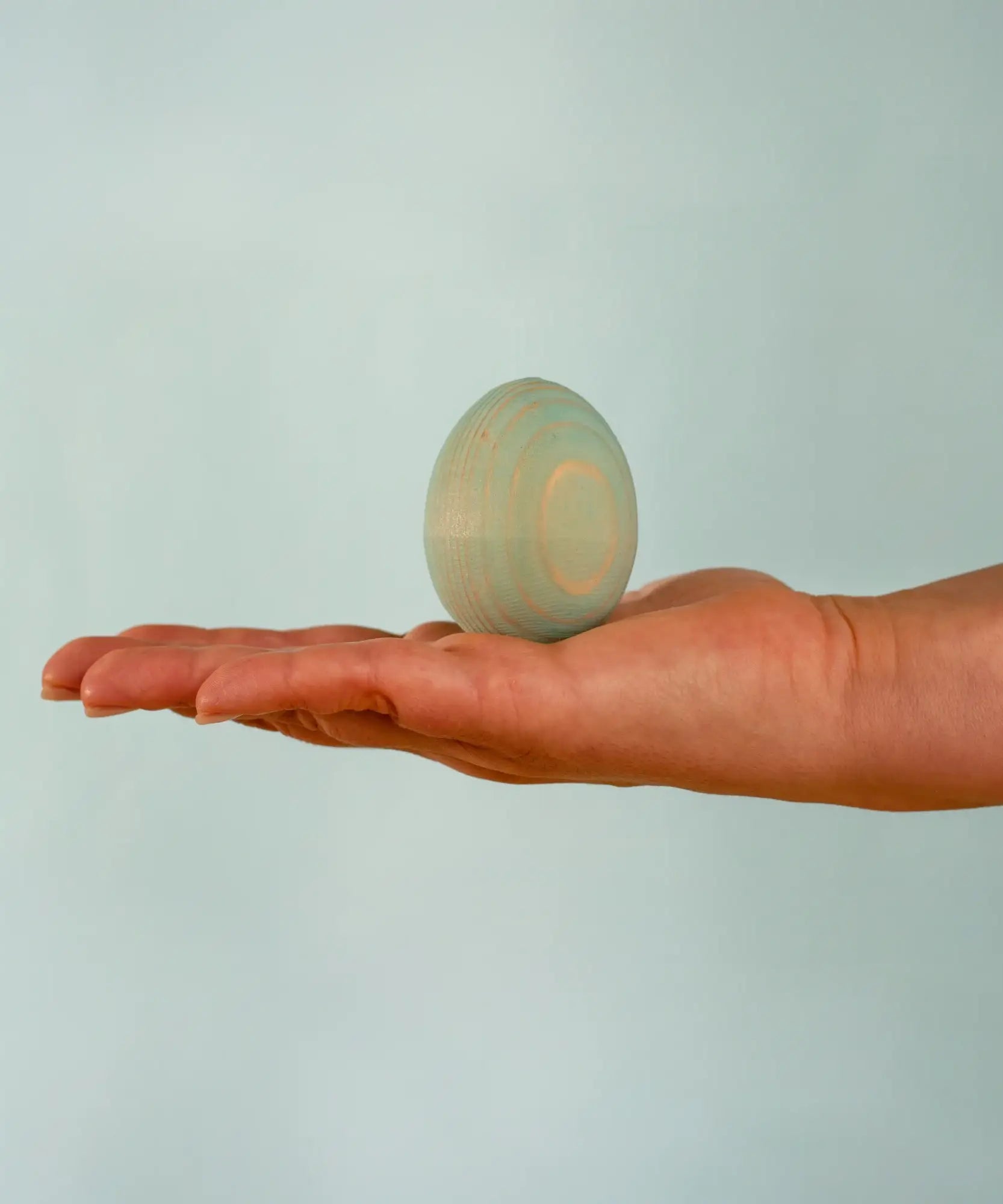 Adult hand holding the Bumbu handcrafted festive blue egg decorative figure showing size