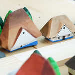 Close up of the Bumbu solid wooden Bucovina house toys on a wooden table next to some grapat mandala trees