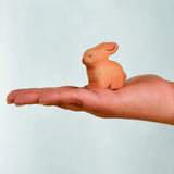 Adult hand holding the Bumbu handcrafted wooden brown rabbit decorative figure showing size