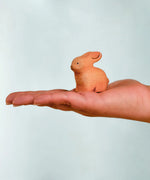 Adult hand holding the Bumbu handcrafted wooden brown rabbit decorative figure showing size