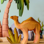 Bumbu handmade wooden camel figure standing in front of desert palm trees