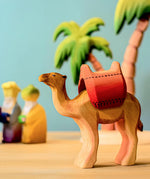 Bumbu wooden camel with red saddle pictured in a small world play scene with three kings and Bumbu palm trees in the background.