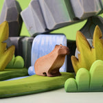Bumbu Toys Wooden Sitting Capybara in a scene with Bumbu rocks and grass.
