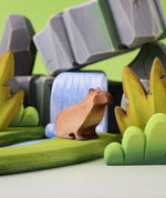 Bumbu Toys Wooden Sitting Capybara in a scene with Bumbu rocks and grass.