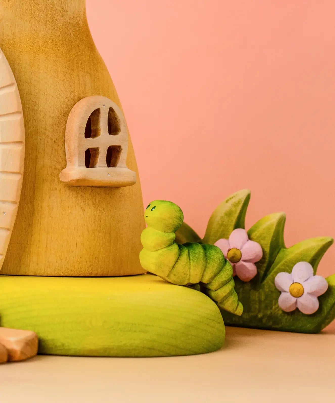 Bumbu wooden green caterpillar on the fairy treehouse base in front of a blossom bush 