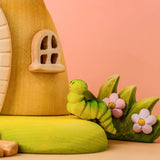 Bumbu wooden green caterpillar on the fairy treehouse base in front of a blossom bush 
