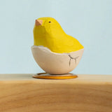 Bumbu wooden hand painted yellow festive chick in egg decorative figure standing in a celebration ring against a blue background