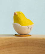 Bumbu wooden hand painted yellow festive chick in egg decorative figure standing in a celebration ring against a blue background