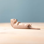 Close up of the Bumbu hand carved sleeping wooden otter toy on a wooden surface in front of a blue background