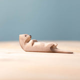Close up of the Bumbu hand carved sleeping wooden otter toy on a wooden surface in front of a blue background