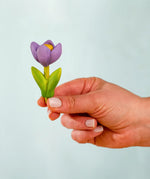 Adult hand holding the Bumbu handcrafted wooden purple crocus decorative figure showing size
