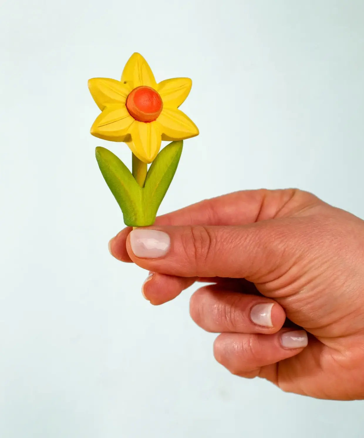 Adult hand holding the Bumbu handcrafted wooden yellow daffodil decorative figure showing size