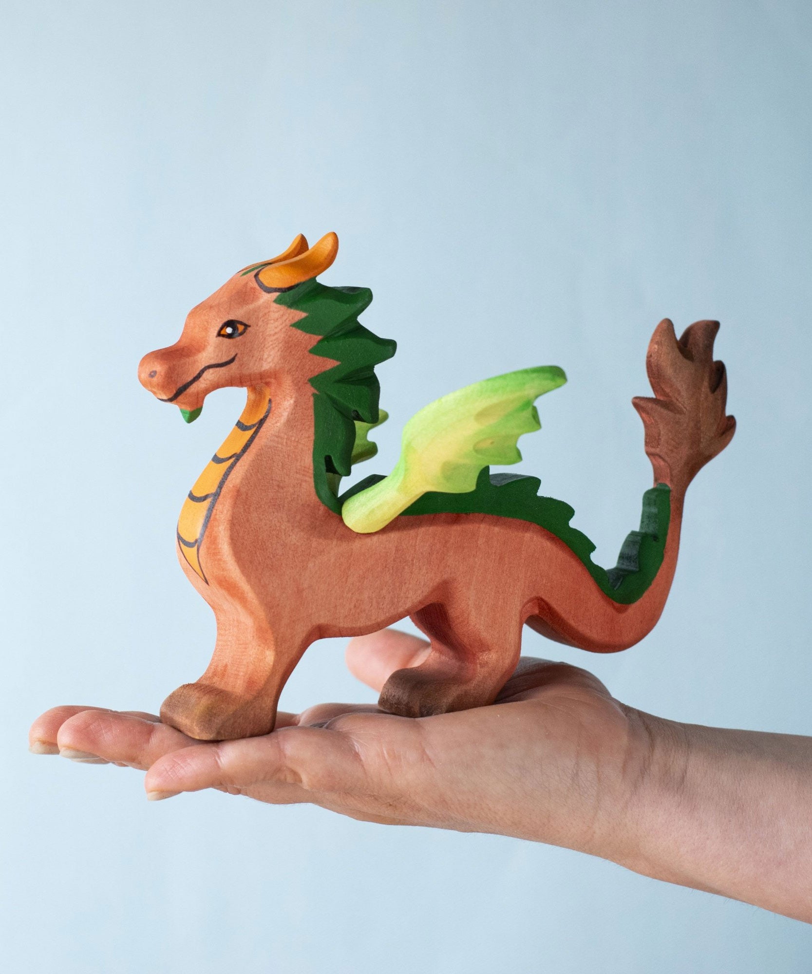 A Bumbu Toys handmade red dragon figure placed on the palm of an adult's hand to show scale. 