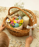 A wicker basket full of Bumbu handcrafted wooden decorative figures including eggs, flowers and a hen