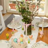 A Easter display showing Bumbu handcrafted wooden eggs, hen, rabbit and spring flower decorative figures on a table with candles