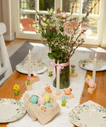 A Easter display showing Bumbu handcrafted wooden eggs, hen, rabbit and spring flower decorative figures on a table with candles