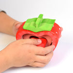Hand slotting together the wooden pieces of the sustainable Bumbu stacking strawberry toy on a white background