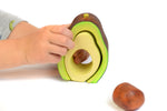 Close up of hands playing with the Bumbu plastic free wooden avocado stacking toy on a white background