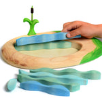 Hand moving the pieces of a Bumbu lake and cattail eco-friendly wooden puzzle on a white background